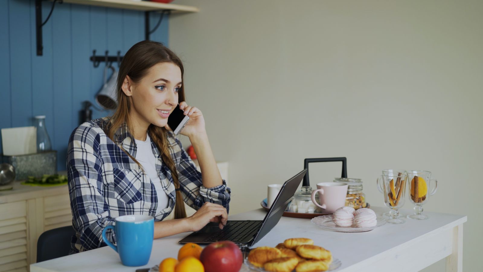 A friendly Village Assistant working on a laptop and phone at her kitchen table