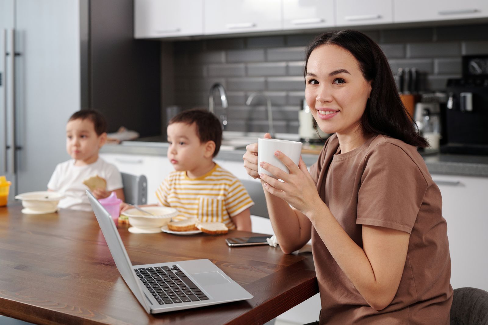 A mother enjoying a coffee at the kitchen table while her children have breakfast nearby